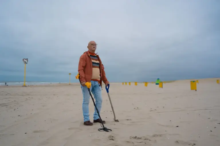 Älterer Mann mit Metalldetektor und Schaufel an einem Strand