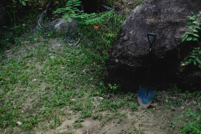 Gartenspaten lehnt an einem Felsen im Gras