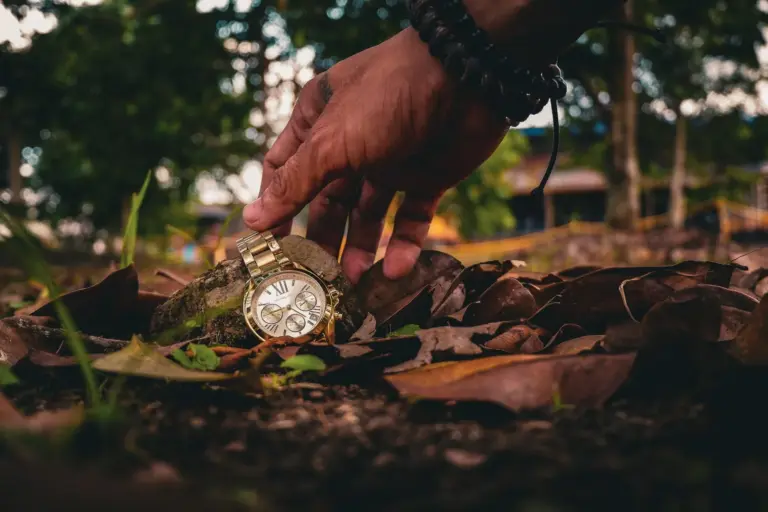 Hand hebt eine Uhr vom Waldboden auf