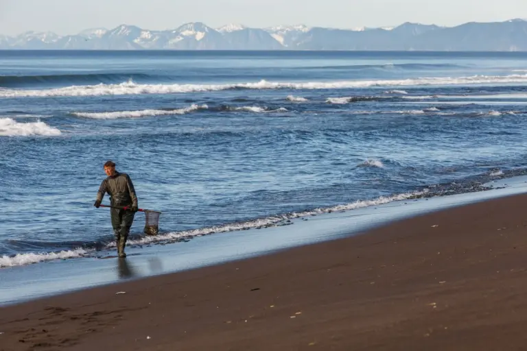 Person mit Ausrüstung am Strand vor Bergen