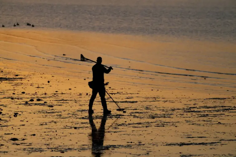 Silhouette eines Mannes mit Metalldetektor am Strand bei Sonnenuntergang