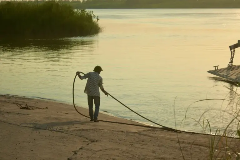 Silhouette eines Mannes zieht am Flussufer ein Seil bei Sonnenuntergang