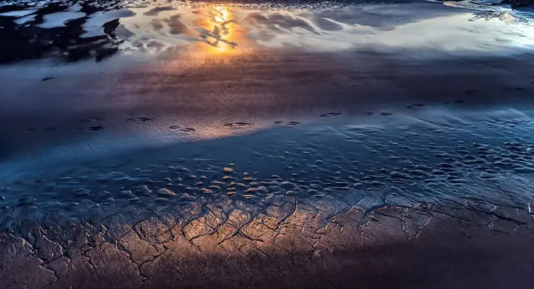 Silhouette eines Sondengängers am Wasser bei Sonnenuntergang