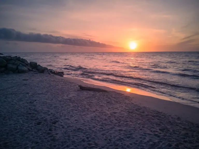 Sonnenuntergang über einem Sandstrand mit ruhigen Wellen
