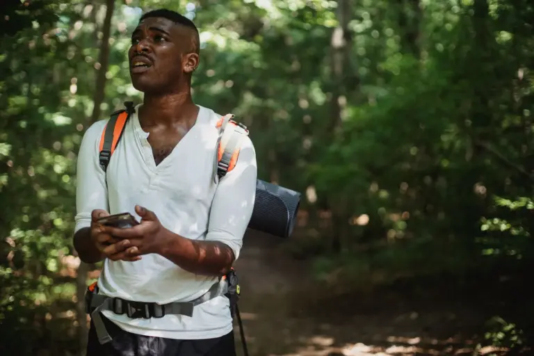 Wanderer mit Rucksack schaut im Wald auf sein Smartphone